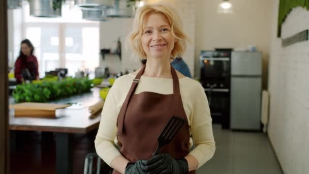 Retrato de mujer adulta alegre sonriendo usando delantal en la clase de cocina en el interior — Vídeo de stock