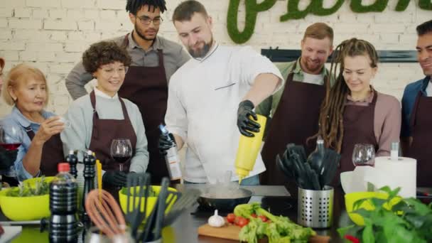 Chef experimentado cocinando carne con fuego mientras los aprendices observan y aplauden — Vídeos de Stock