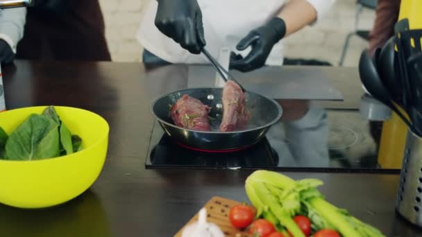 Kompetent manlig kock matlagning kött i stekpanna arbetar med grupp av människor — Stockvideo