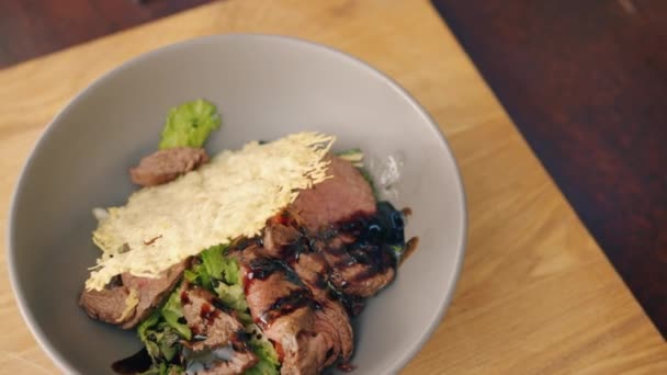 Detailní záběr misky z vařeného masa a zeleniny na dřevěném stole v kuchyni — Stock video