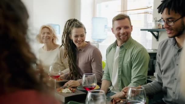 Разнообразная группа взрослых болтает и смеется сидя за столом с едой и напитками — стоковое видео