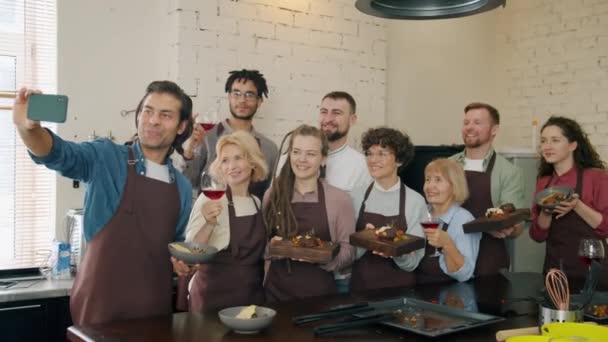 Férfiak és nők, akik ételt és italt tartanak, főzés után okostelefonnal szelfiznek — Stock videók