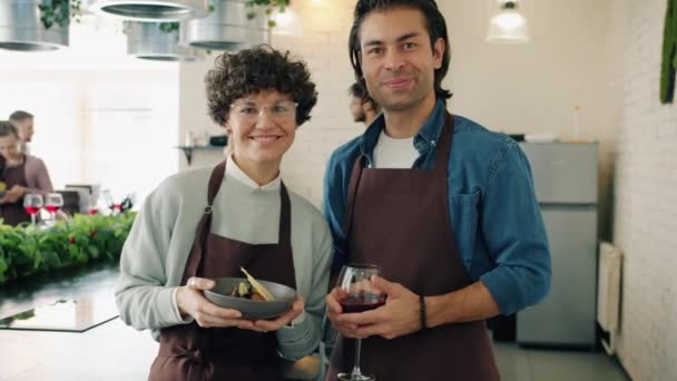 Retrato en cámara lenta del hombre y la mujer en clase de cocina sosteniendo comida y bebida sonriendo — Vídeos de Stock