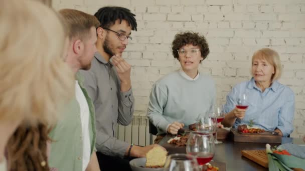 Медленное движение людей, говорящих сидя за столом с едой и напитками в помещении — стоковое видео