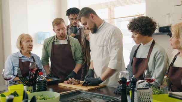 Långsamma rörelser av människor tittar på kock matlagning måltid under matlagning klass prata — Stockvideo