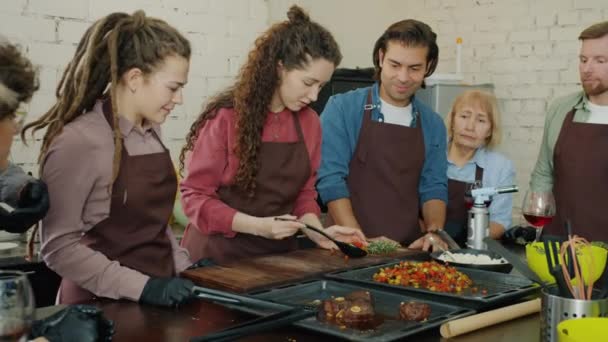 Joyful jonge vrouw koken maaltijd met groep van culinaire klasse studenten in de keuken — Stockvideo