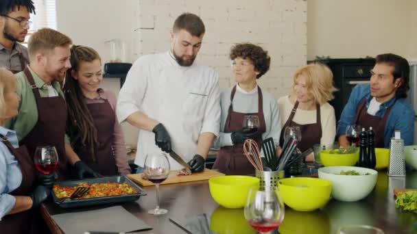 Bello giovane chef taglio carne fritta insegnamento gruppo di persone abilità di cucina — Video Stock