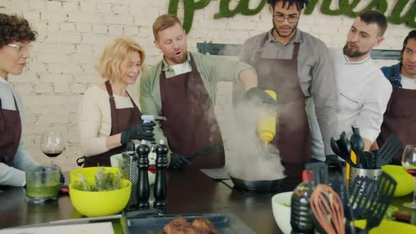 Movimiento lento de hombres y mujeres cocinando carne con fuego en clase de cocina bajo la guía del chef — Vídeo de stock