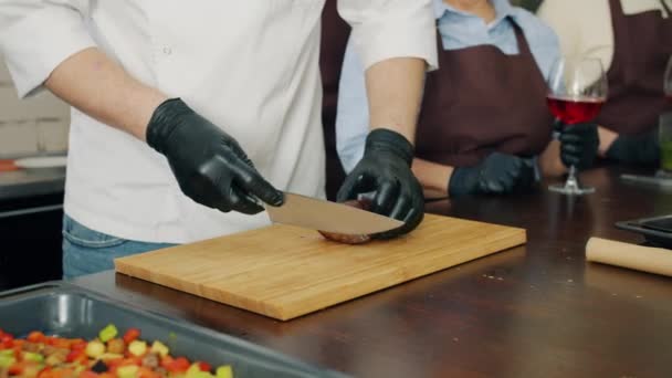 Närbild av kock skära stekt kött bit i kök lärargrupp av studenter — Stockvideo