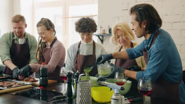 Groupe multi-racial d'étudiants en cours de cuisine préparant des repas en cuisine discutant avec le chef — Video