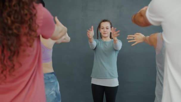 Bella ragazza che insegna yoga in classe facendo esercizi di riscaldamento con gruppo di persone — Video Stock