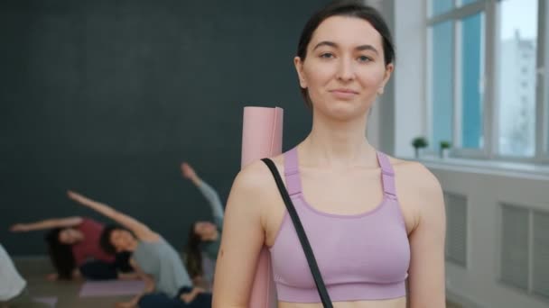 Portrét dobře vypadající mladé brunetky ve sportovním oblečení stojící ve studiu jógy s úsměvem — Stock video