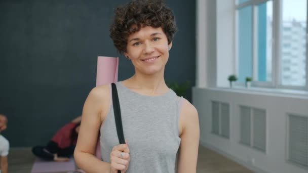 Портрет красивої молодої жінки в студії йоги посміхається дивитися на камеру — стокове відео