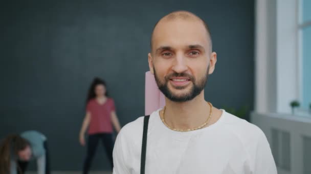 Portret atrakcyjnego ucznia jogi facet uśmiecha się w studio trzymając matę patrząc w kamerę — Wideo stockowe