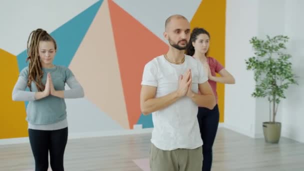 Grupo de jóvenes haciendo ejercicios durante clases de yoga en interiores en estudio — Vídeos de Stock