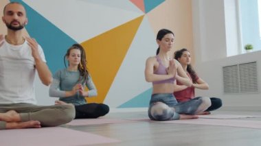 Kızlar ve erkek yoga antrenmanında meditasyon yaparken rahat stüdyoda lotus pozunda oturuyorlar.