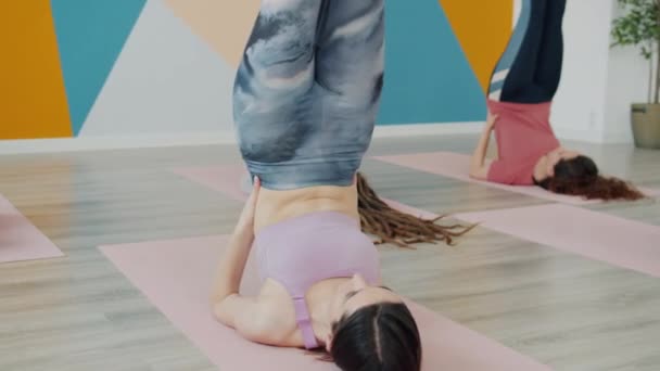 Attraktive schlanke Frauen beim Yoga im Studio auf Matten liegend mit hochgestellten Beinen in Sportbekleidung — Stockvideo