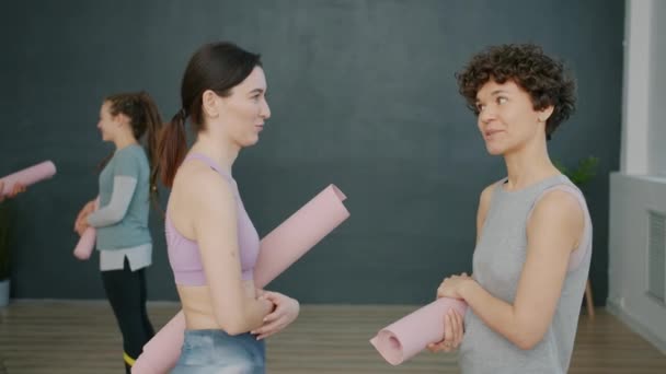 Hermosas mujeres jóvenes hablando en estudio de yoga riendo divirtiéndose juntas — Vídeo de stock