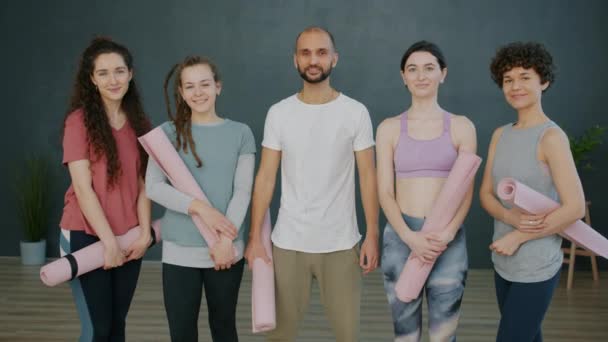 Портрет счастливой молодежи мужчины и женщины, улыбающиеся в студии йоги с ковриками в руках — стоковое видео