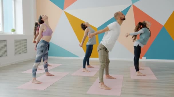 Grupo de jóvenes en ropa deportiva flexión hacia adelante durante la práctica de yoga — Vídeo de stock