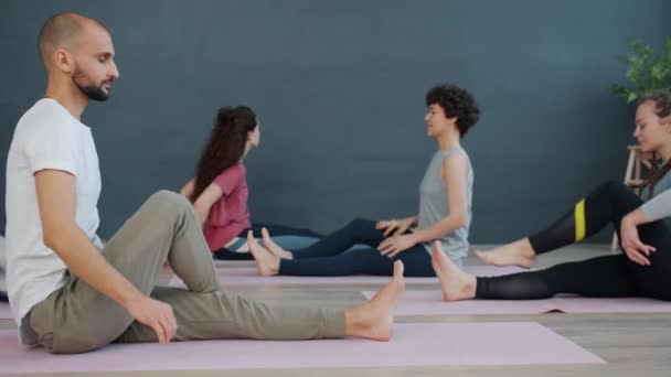 Dziewczyny i facet korzystających jogi praktyki w światło pokój siedzi na maty razem — Wideo stockowe