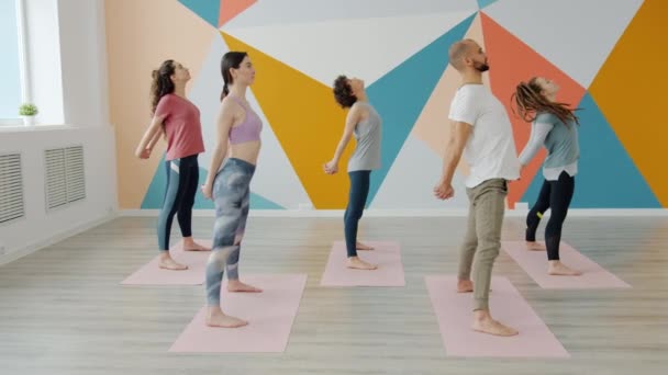 Chicas y chico haciendo yoga en estudio moderno doblando hacia adelante estirando el cuerpo — Vídeo de stock