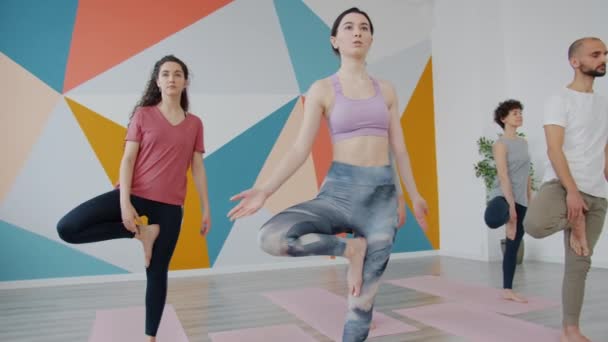 Nők és férfiak komoly emberek jógáznak fél lábon a stúdióban — Stock videók
