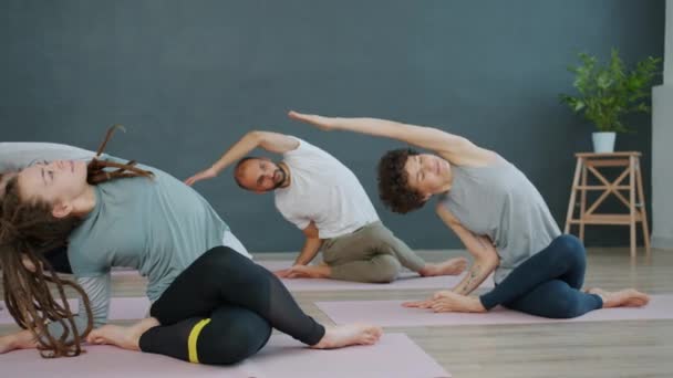 Gomukhasana pozisyonunu bir grup insana gösteren yoga eğitmeni konuşuyor. — Stok video