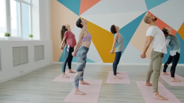 Lento movimiento de chico y chicas jóvenes practicando yoga en estudio doblando hacia adelante — Vídeos de Stock