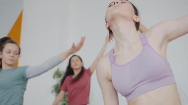 Красивая гибкая девушка в модном спортивном топе занимается в студии йоги с группой людей — стоковое видео