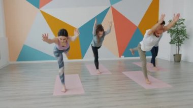 Yoga stüdyosunda yavaş hareket eden gençler paspaslar üzerinde asma dengeliyor.