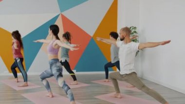 Erkek ve kadın savaşçı pozisyonunda yoga stüdyosunda birlikte egzersiz yapıyorlar.