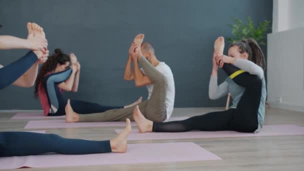 Attraktiva kvinnor och man som gör yoga i klass stretching ben sitter på mattor — Stockvideo