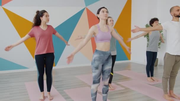 Mujeres y hombres en ropa deportiva haciendo yoga equilibrando asanas en club deportivo — Vídeos de Stock