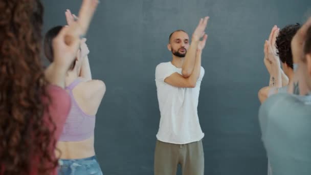 Привабливий хлопець тренер йоги розмовляє з групою студентів-жінок, які займаються в приміщенні — стокове відео