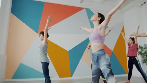 Les filles et le gars se penchent en avant pendant la pratique du yoga dans la formation de gymnastique spacieuse ensemble — Video