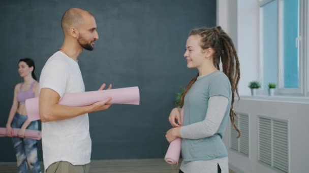 Dívka a chlap držící rohože mluví a gestikulace stojící ve sportovním centru — Stock video