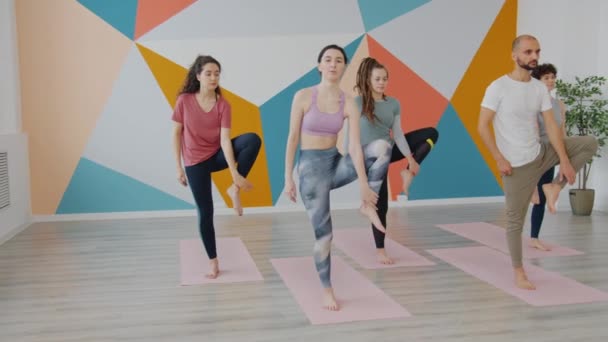 Jóvenes estudiantes disfrutando de la relajación en clase de yoga haciendo posición de árbol equilibrando asana — Vídeos de Stock