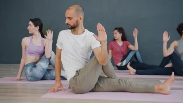 Junge Männer und Frauen mit Yoga-Asanas beschäftigt, die auf Matten im hellen Studio sitzen — Stockvideo