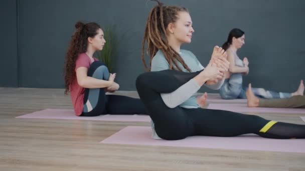 Grupo de adultos haciendo ejercicios de estiramiento de yoga en estudio moderno sentados en esteras — Vídeos de Stock