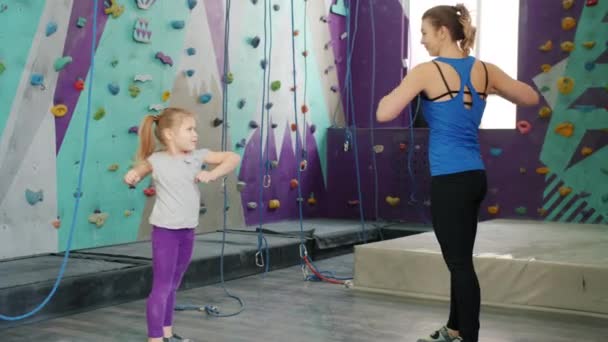 Niña haciendo ejercicio en el interior en el gimnasio de escalada con la madre cariñosa torcer el cuerpo — Vídeos de Stock