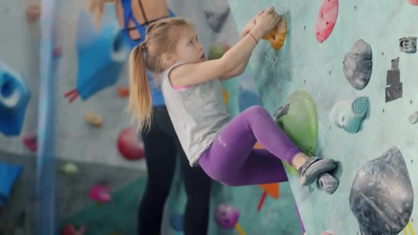 Adorable niña subiendo por colorido entrenamiento de pared artificial en el gimnasio interior — Vídeos de Stock