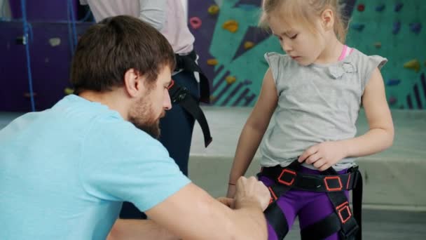 Instrutor de escalada amigável ajudando a criança com arnês de segurança dentro de casa no ginásio — Vídeo de Stock
