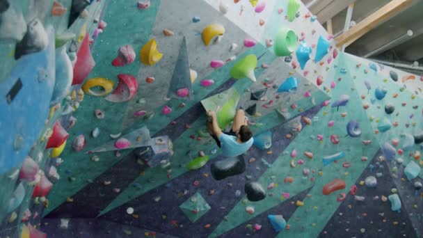 Guy climbing up artificial wall then falling on crash mat in indoor sports facility — Stock Video