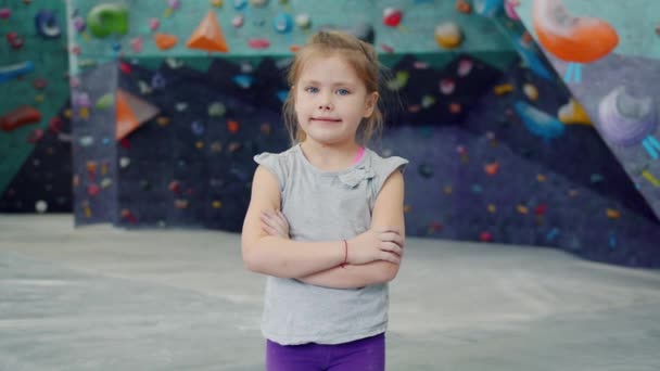 Πορτρέτο του όμορφου μικρού κοριτσιού σε εσωτερικούς χώρους αναρρίχηση εγκατάσταση στέκεται μόνη της κοιτάζοντας κάμερα — Αρχείο Βίντεο