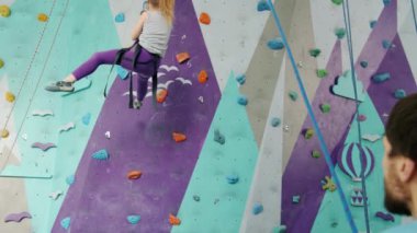 Yavaş çekimde çocuk tırmanma duvarından aşağı iniyor. Eğitmenle birlikte ipe asılıyorlar.