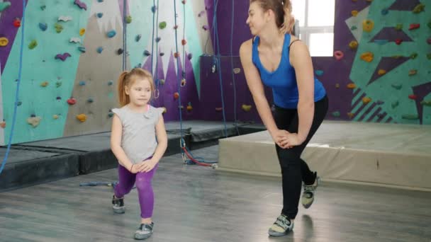 Young woman and little girl exercising indoors in climbing club near artificial wall — Stock Video