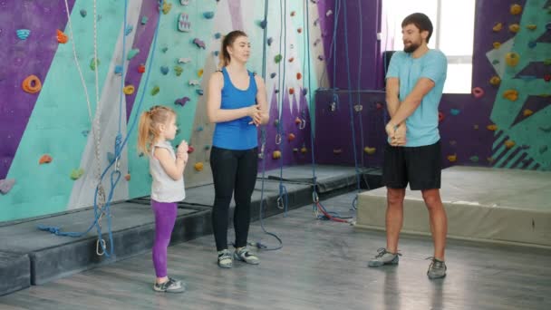 Чоловік і жінка тренуються в тренажерному залі для скелелазіння з маленькою дочкою зігріваючими руками — стокове відео