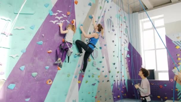 Woman and kid enjoying climbing in gym while companions holding ropes standing below — Stock Video