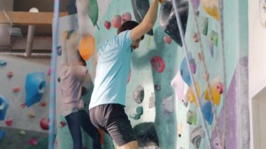 Erkek ve kadın kaya tırmanışı tesisinde antrenman yapıyor, içeride antrenmanların keyfini çıkarıyor.